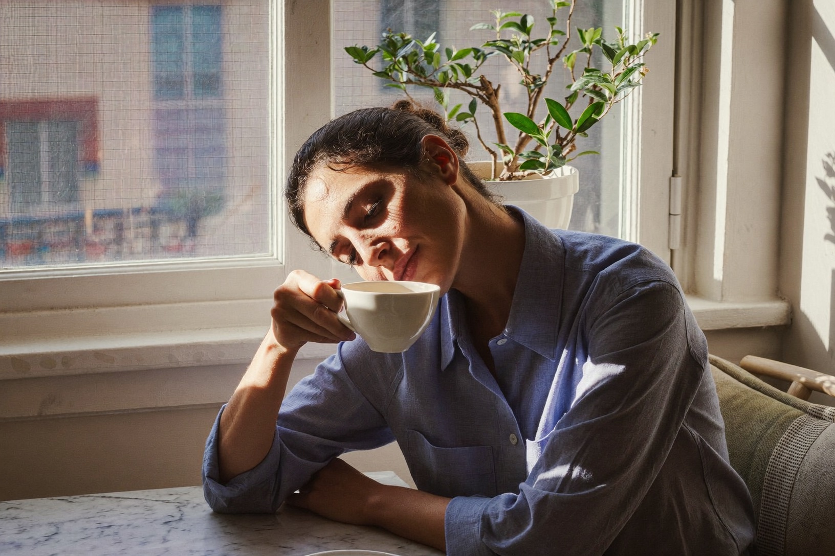 Frau sitzt nachdenklich mit einer Tasse Tee am Fenster